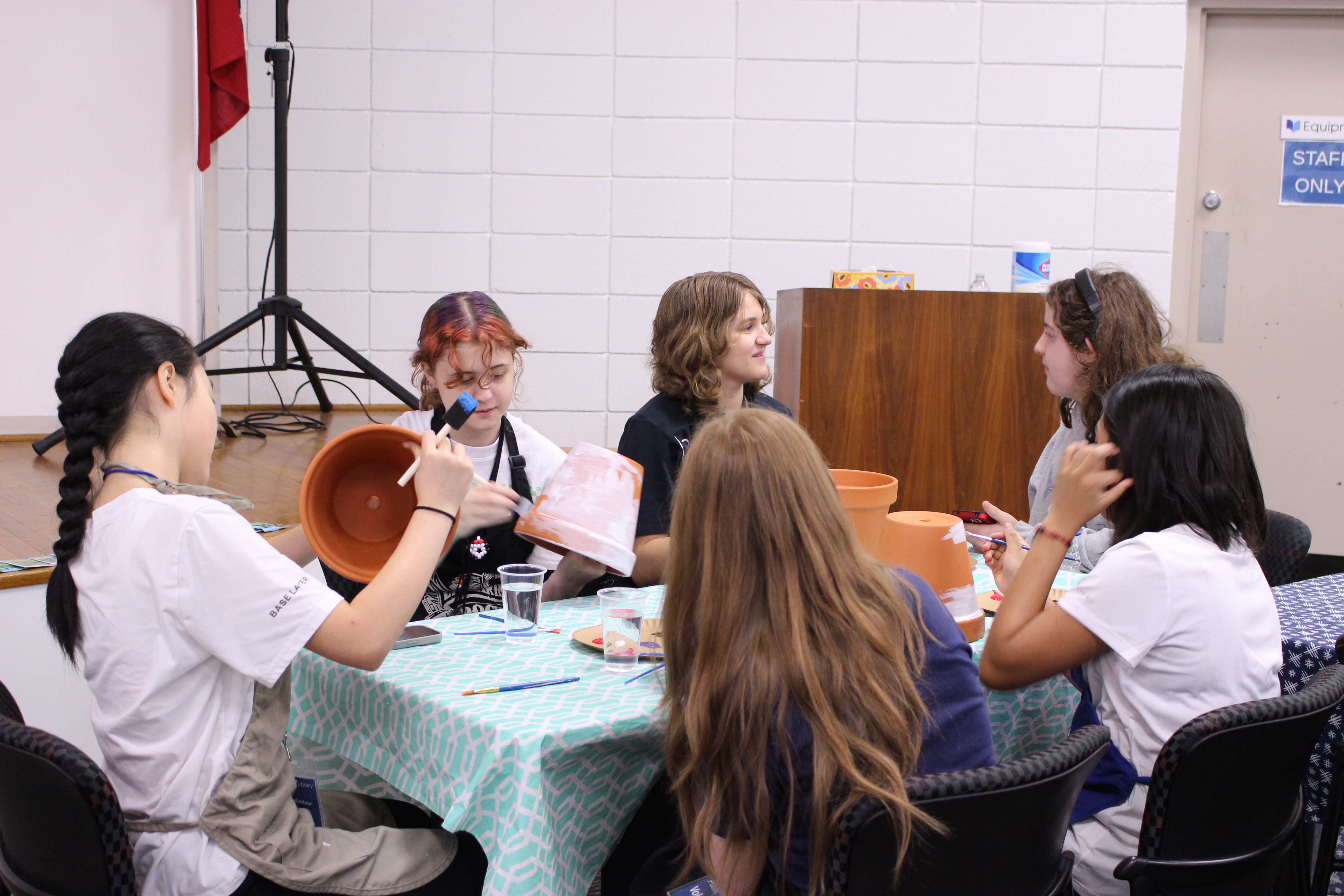 Group of teens sitting at a table painting terracotta plant pots and chatting